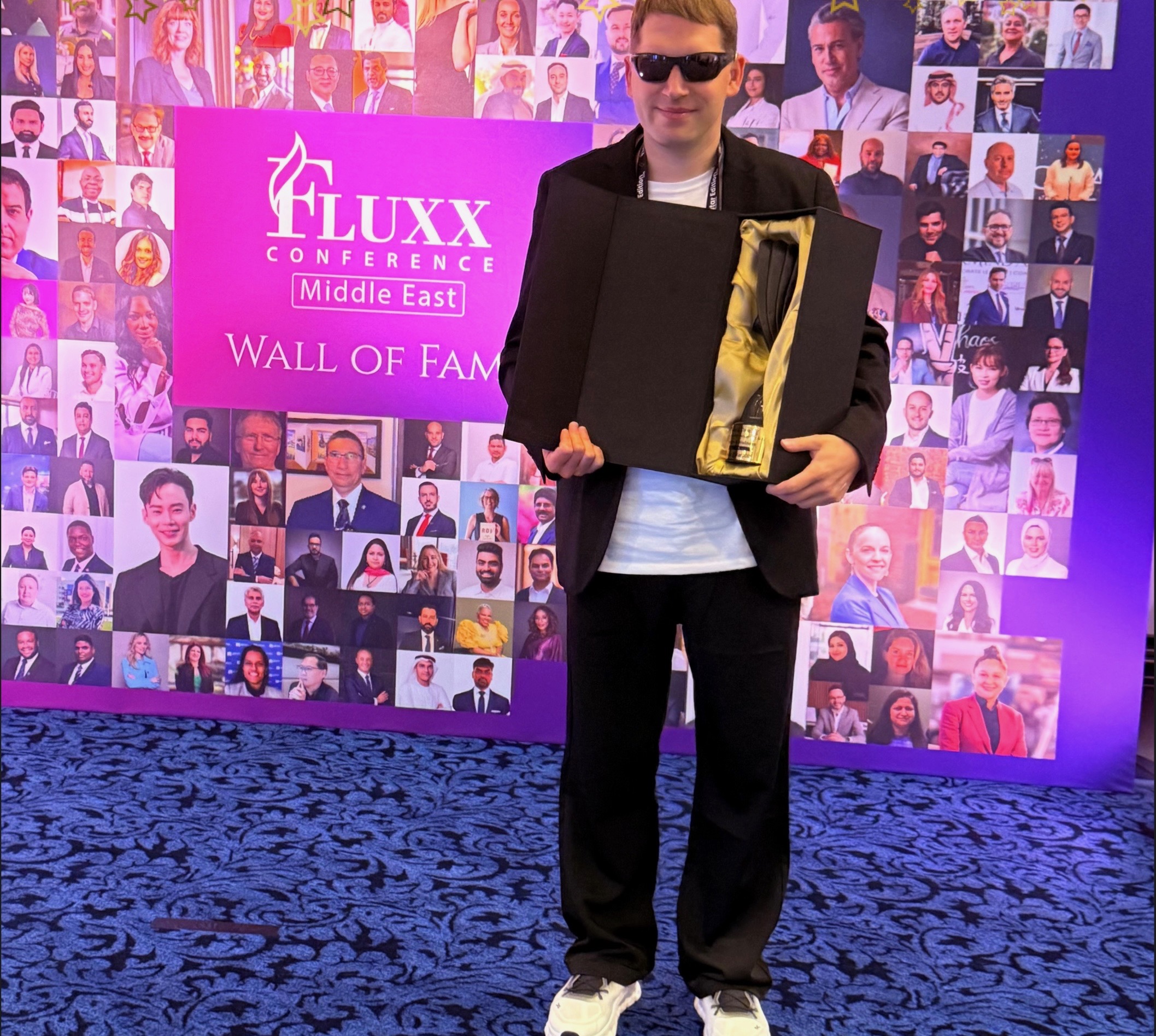 Professional standing at an international conference holding an award in front of a recognition display.
